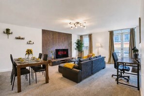 A modern living room with a dining area, a sofa, a TV, and a plant.