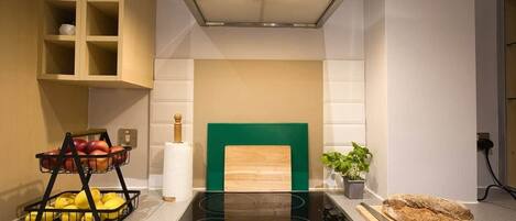 A kitchen with a built-in stove, a wooden cutting board, and a fruit basket.