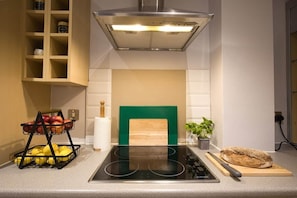 A kitchen with a built-in stove, a wooden cutting board, and a fruit basket.