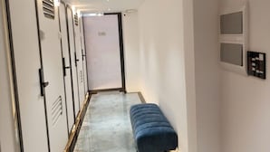 Un pasillo con un banco, puertas, un extintor y un panel de control en la pared.