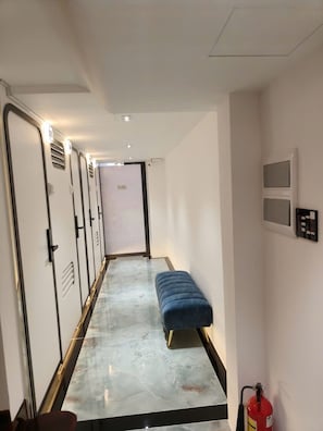 A hallway with a bench, doors, a fire extinguisher, and a wall-mounted control panel.