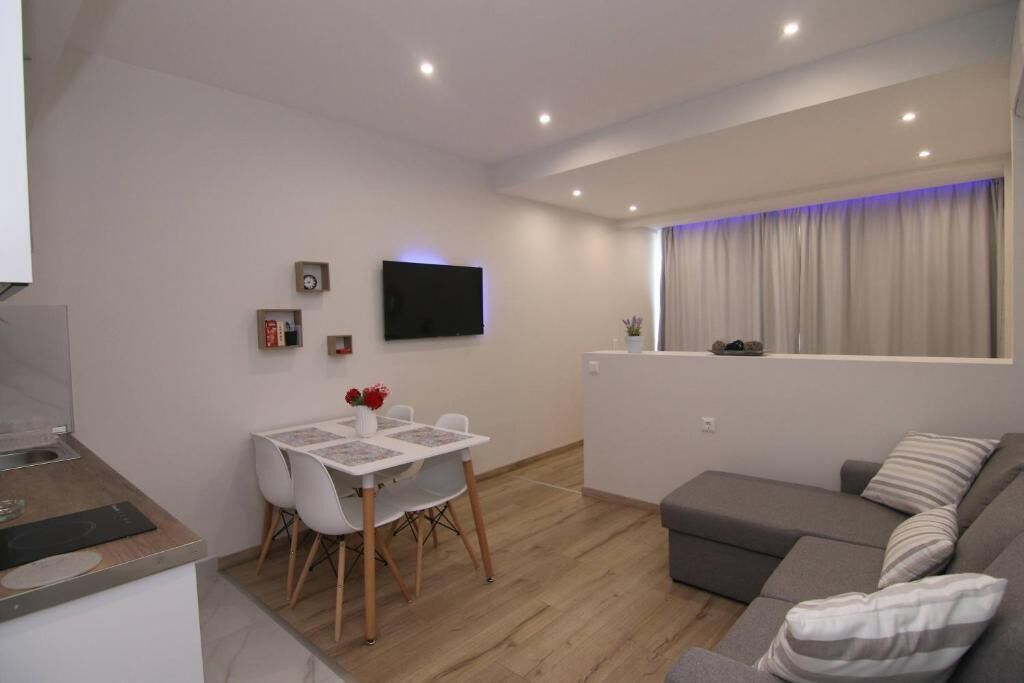 Een moderne woonruimte met een eethoek, een bank, een flatscreen televisie en een raam met gordijnen.