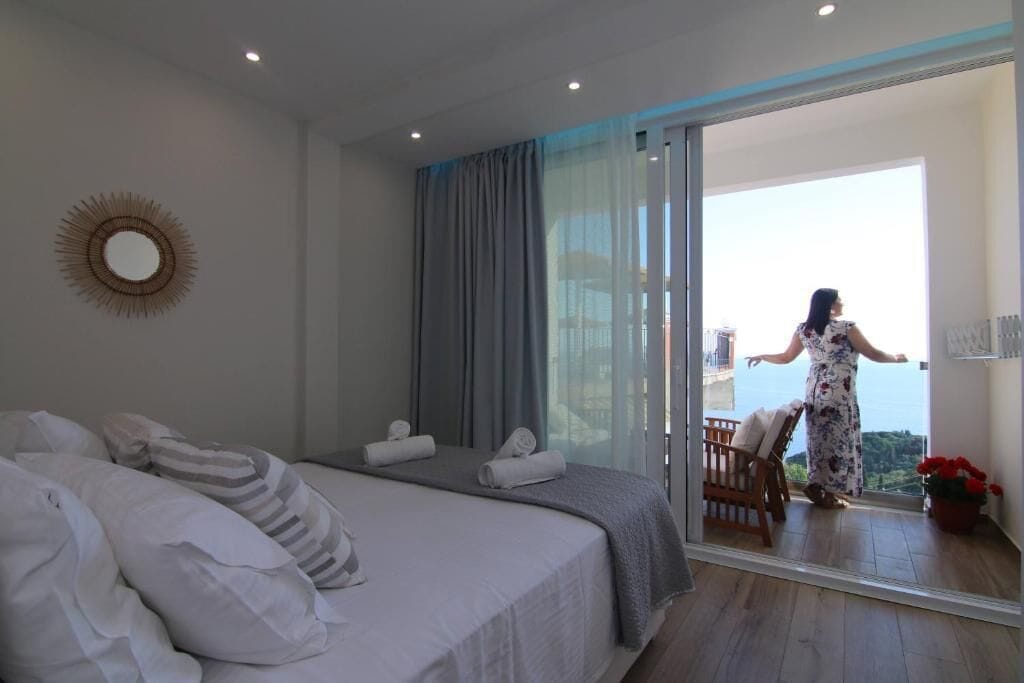 A bedroom with a bed, a large mirror, and a balcony with a view.