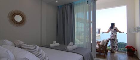 A bedroom with a bed, a large mirror, and a balcony with a view.