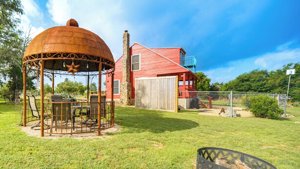 Um gazebo com decoração em estrela, um edifício vermelho com porta de madeira e um quintal cercado.
