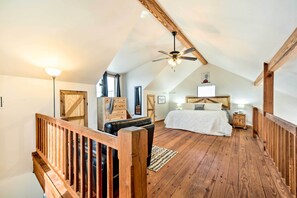 Ein Schlafzimmer mit schrägen Wänden, Holzbalken, einem Bett, einem Nachttisch und einem Deckenventilator.