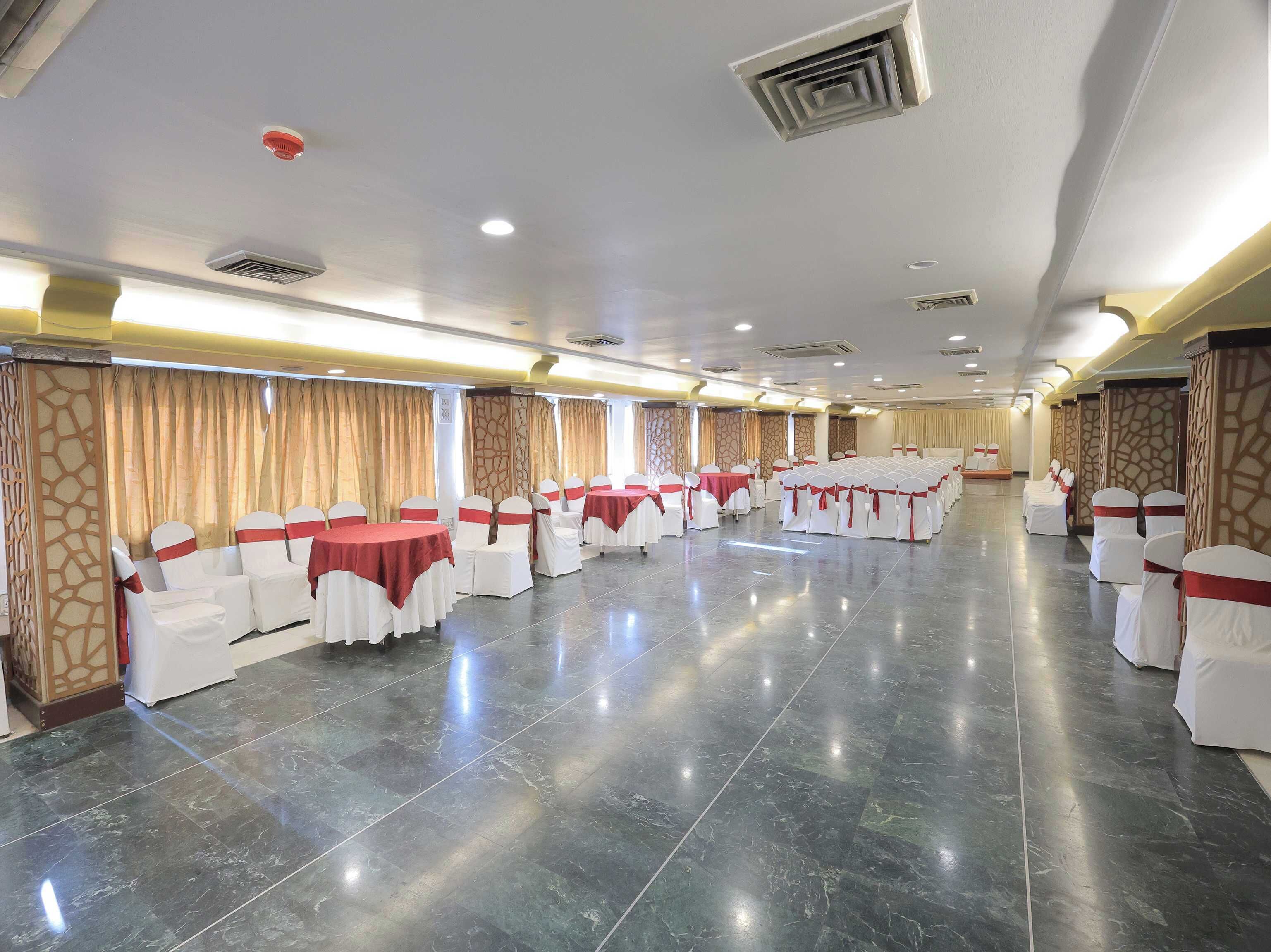 A banquet hall with rows of tables and chairs, equipped with ceiling lights and ventilation.