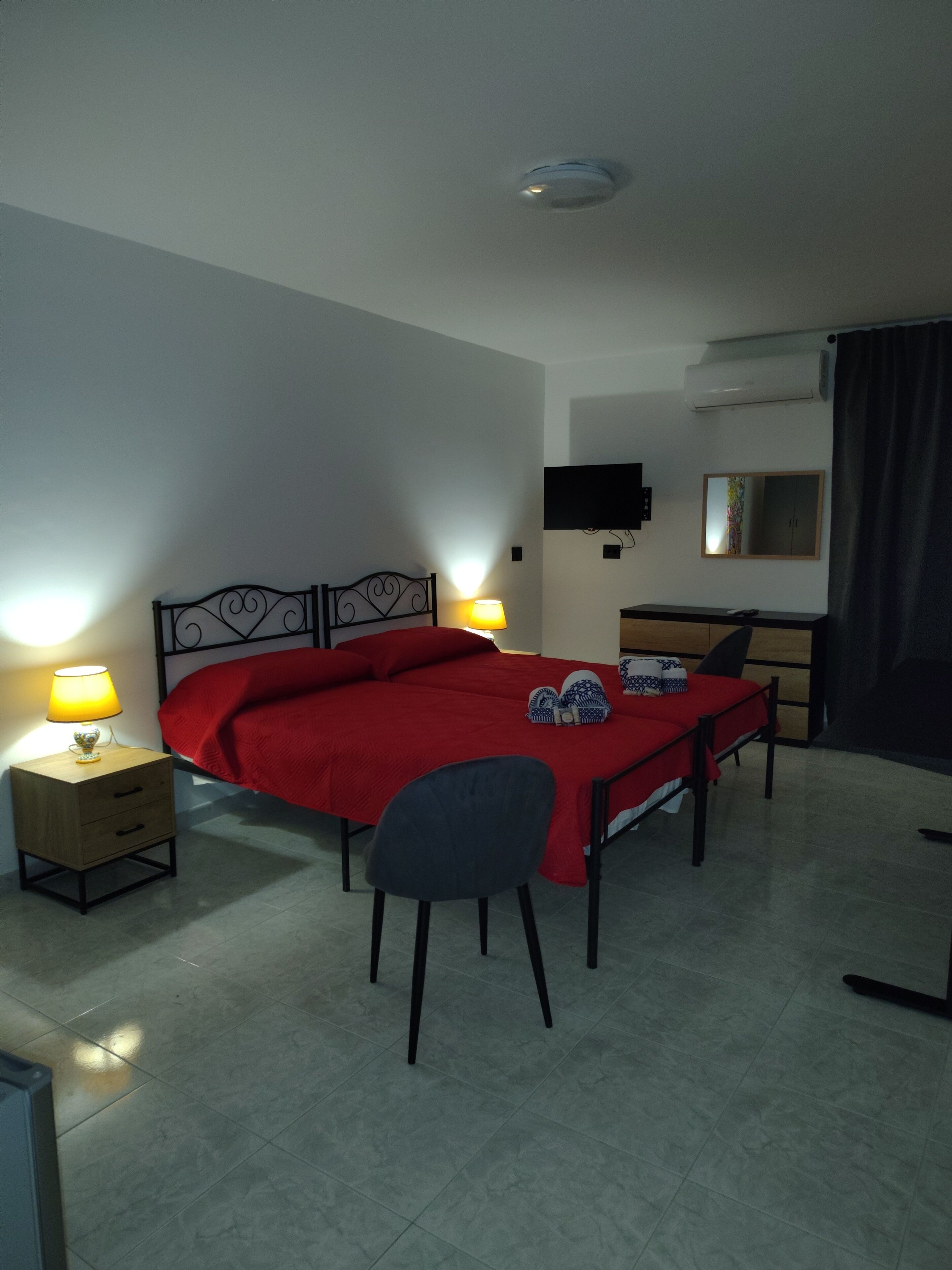 Ein Schlafzimmer mit Bett, Nachttischen, einem Sessel, einem Fernseher und einer Klimaanlage.