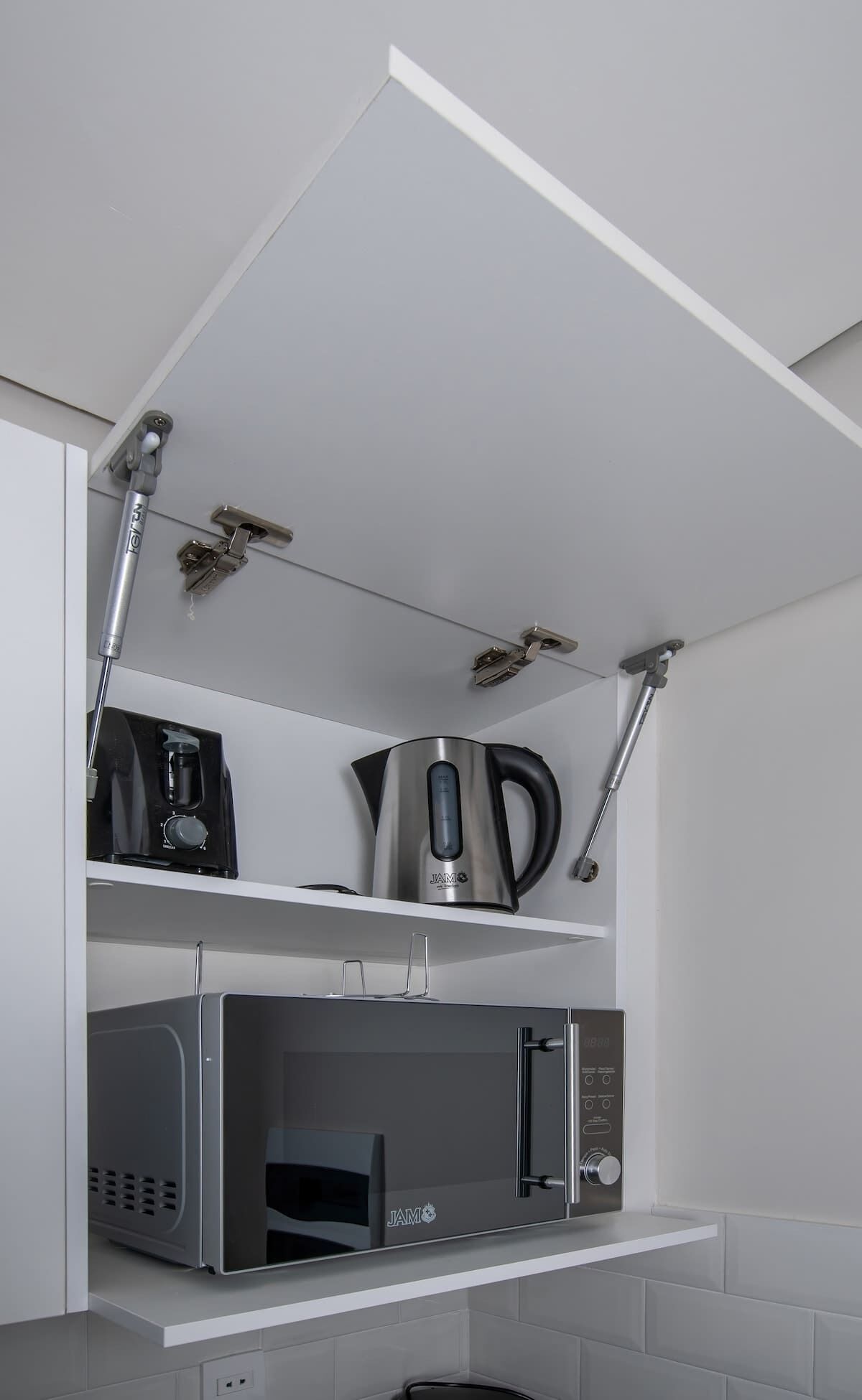Een keuken met een magnetron, koffiezetapparaat en waterkoker op een wit aanrecht.