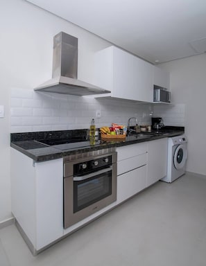 Una cocina moderna con armarios blancos, estufa de acero inoxidable, horno integrado, microondas y lavadora.