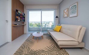 Ein modernes Wohnzimmer mit einer Couch, einem Couchtisch, einem an einer Holzvertäfelung montierten Fernseher und einem großen Fenster mit Blick.
