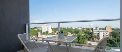 Un balcón con una mesa y dos sillas, con vistas a un paisaje urbano con edificios y zonas verdes.