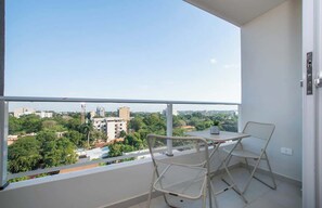 Ein Balkon mit Tisch und Stühlen, mit Blick auf eine Stadtlandschaft aus Gebäuden und Grünflächen.
