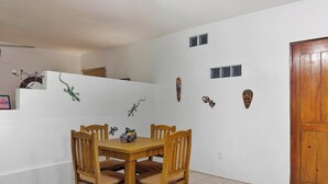 Un comedor con una mesa y sillas de madera, una pared blanca con máscaras decorativas y una puerta de madera.
