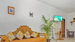 Una sala de estar con un sofá, un televisor, una planta en maceta y un cuadro en la pared.