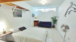 Un dormitorio con cama, mesita de noche, lámpara, ventilador, sofá, puerta y un cuadro en la pared.