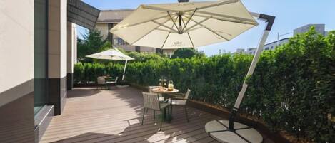 An outdoor patio with a wooden deck, two umbrellas, and a table with chairs.