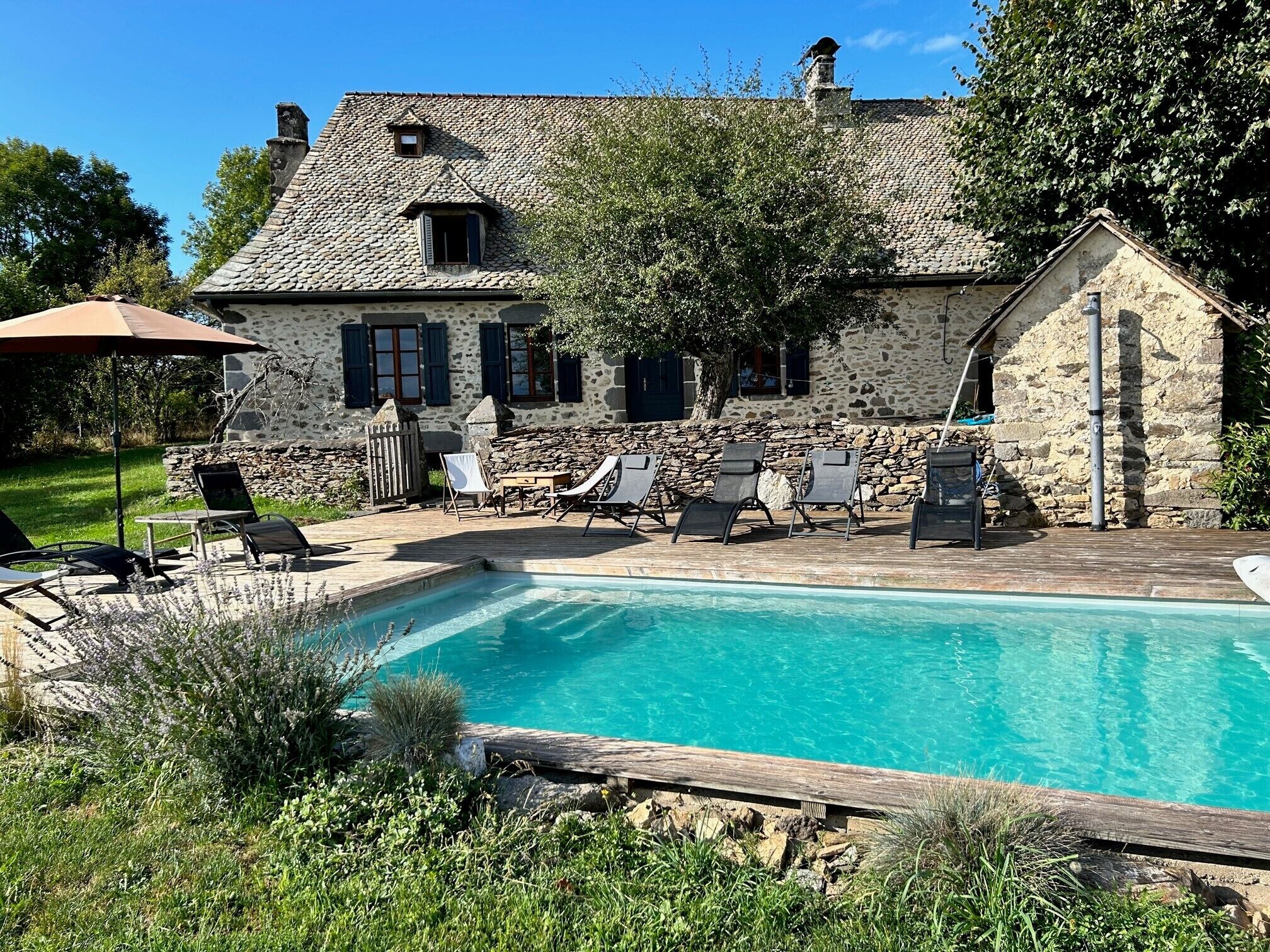 Une maison en pierre avec une piscine, un espace salon extérieur et un jardin.