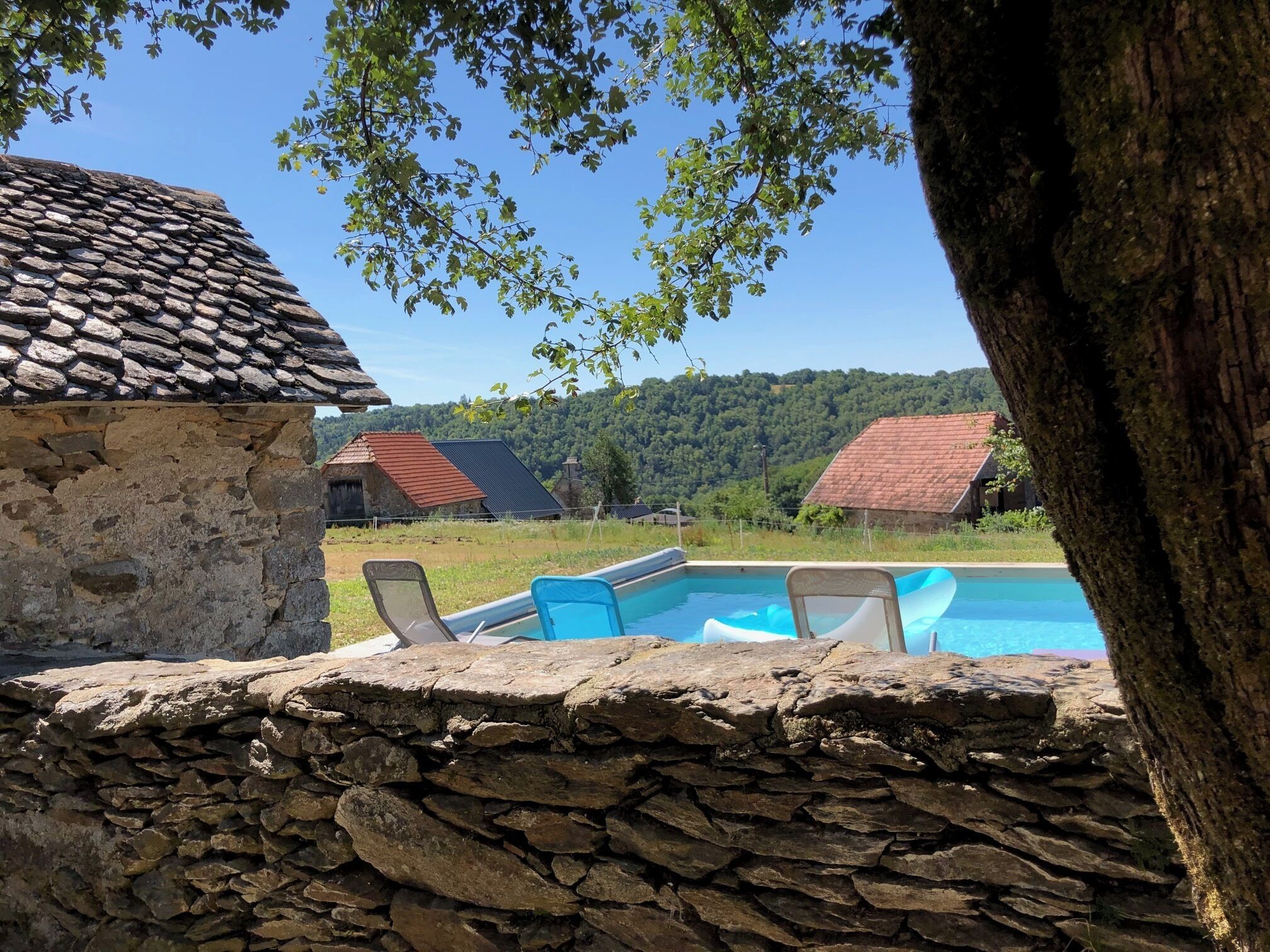 A stone wall, a swimming pool with lounge chairs, and a view of a forested hill.