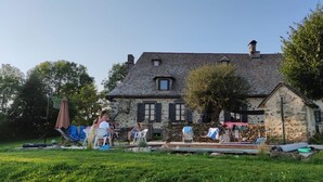 A stone house with a sloped roof, a small balcony, and a tree in the yard. - Large Auvergne-style house with a pool, pétanque court, and bread oven (Saint-Martin-Cantalès)