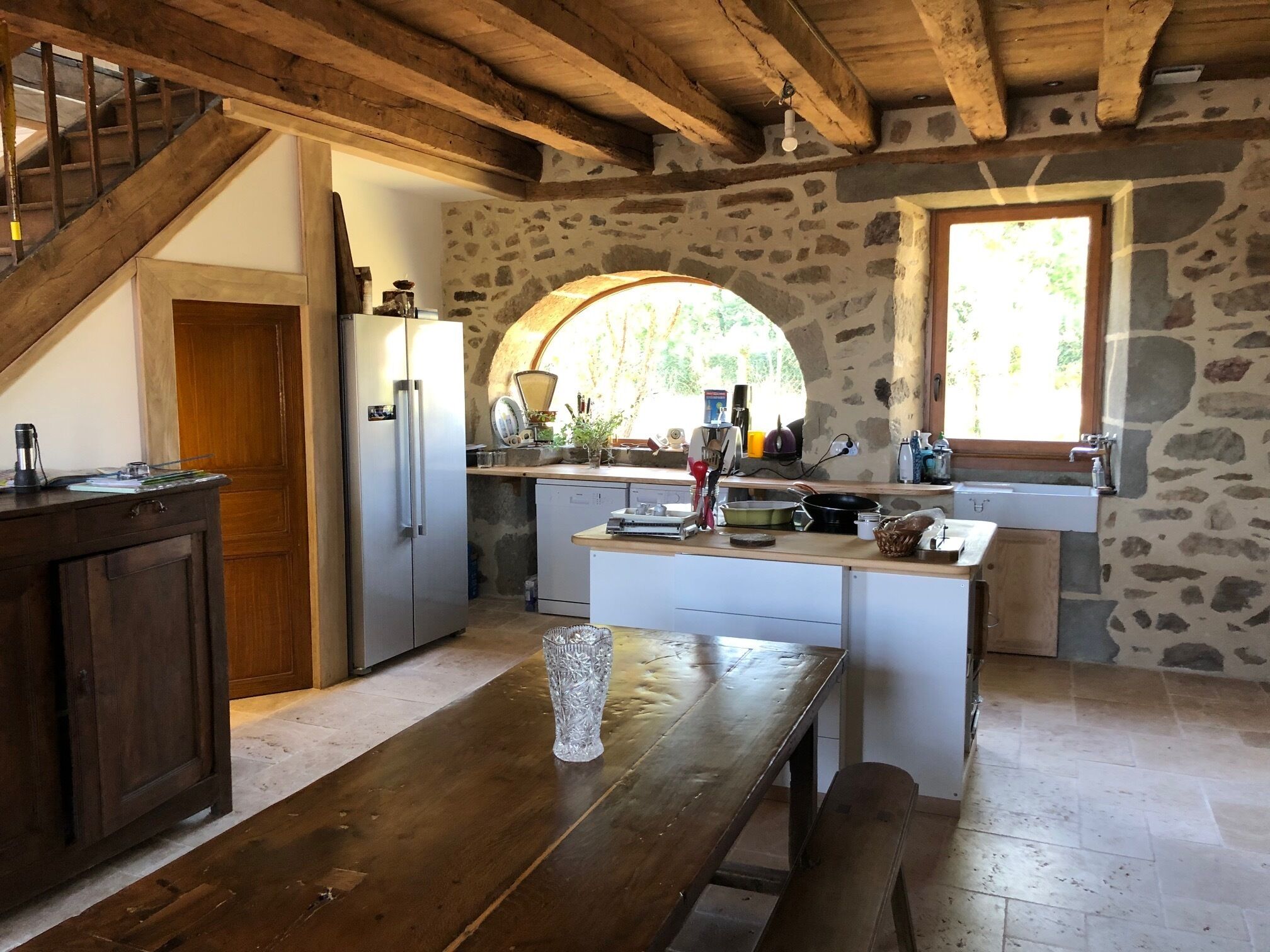 Una cocina rústica con una mesa de madera, un refrigerador y una pared de piedra.