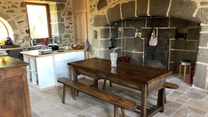 A rustic kitchen with a stone wall, wooden table, and bench. - Large Auvergne-style house with a pool, pétanque court, and bread oven (Saint-Martin-Cantalès)