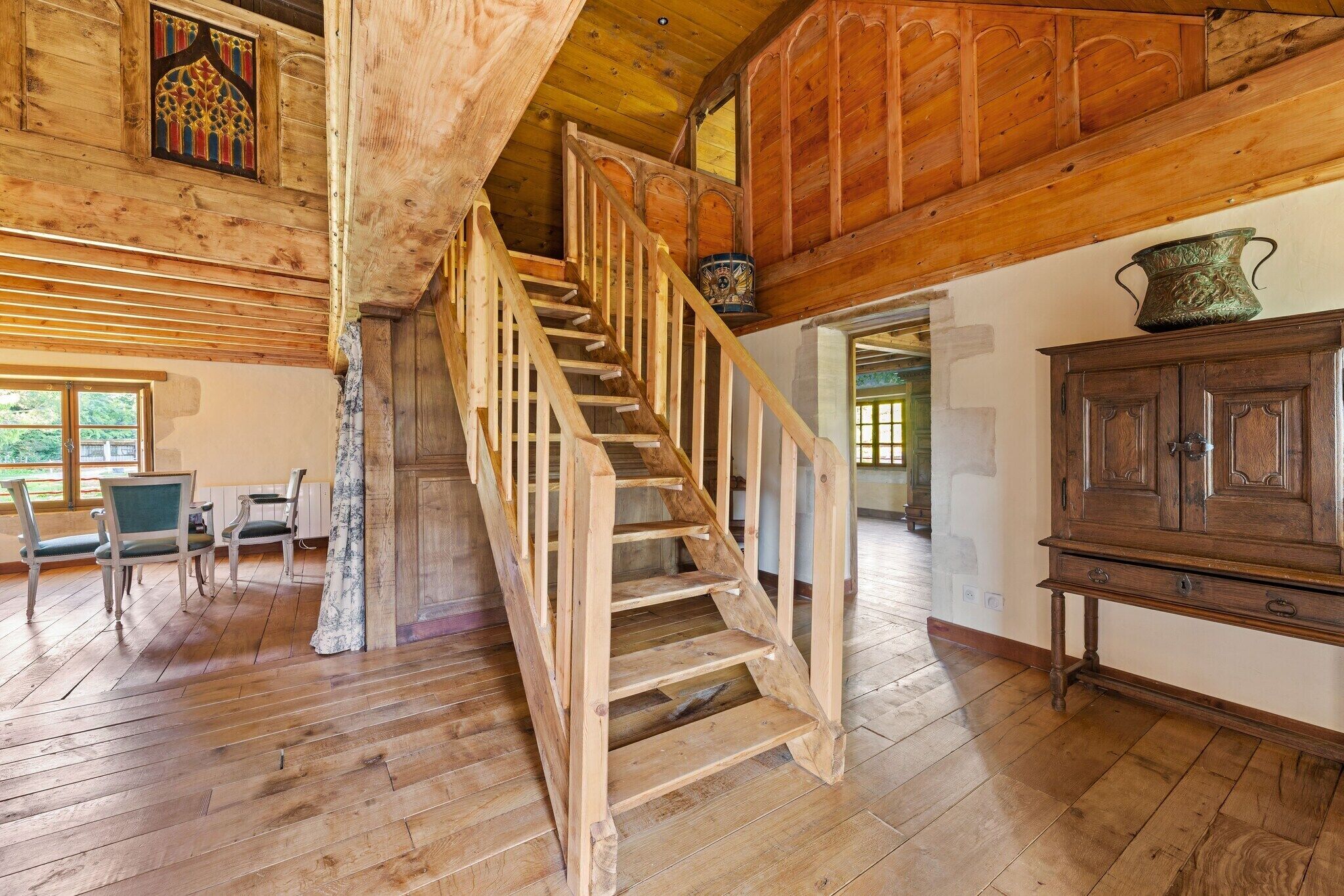 A wooden staircase leading to an upper level, a dining area with chairs and a table, and a large cabinet with decorative items.
