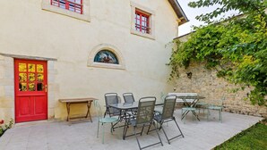 A building with a red door, a stone wall, and a patio with outdoor furniture. - Holiday Home in Le Manoir with Jacuzzi in summer (Le Manoir)
