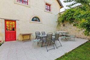 Ein Gebäude mit roter Tür, einer Steinwand und einer Terrasse mit Gartenmöbeln.