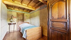A wooden bed in a room with a wooden ceiling, a small table with a lamp, and a wooden door. - Holiday Home in Le Manoir with Jacuzzi in summer (Le Manoir)