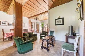 A room with a wooden ceiling, green upholstered furniture, a wooden table, and a television on a stand. - Holiday Home in Le Manoir with Jacuzzi in summer (Le Manoir)