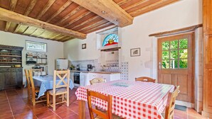 A rustic kitchen with wooden beams, a dining table with checkered tablecloths, and a view through a window. - Holiday Home in Le Manoir with Jacuzzi in summer (Le Manoir)