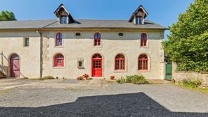 A two-story building with a symmetrical facade, a central red door, and multiple windows with red frames. - Holiday Home in Le Manoir with Jacuzzi in summer (Le Manoir)