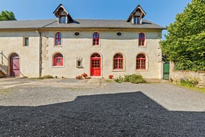 A two-story building with a symmetrical facade, a central red door, and multiple windows with red frames.