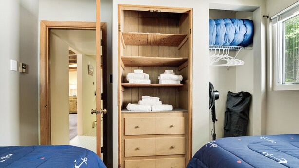 Un dormitorio con dos camas, un armario de madera, una ventana y una puerta que da a otra habitación.