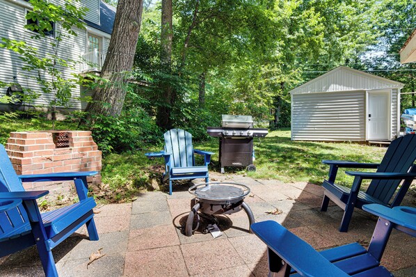 A backyard with a grill, chairs, and a shed.