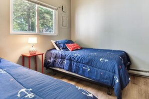 A bedroom with two beds, a window, and a lamp.