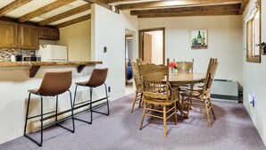 Una cocina con vigas de madera, un refrigerador y un microondas. Hay un comedor con una mesa y sillas.