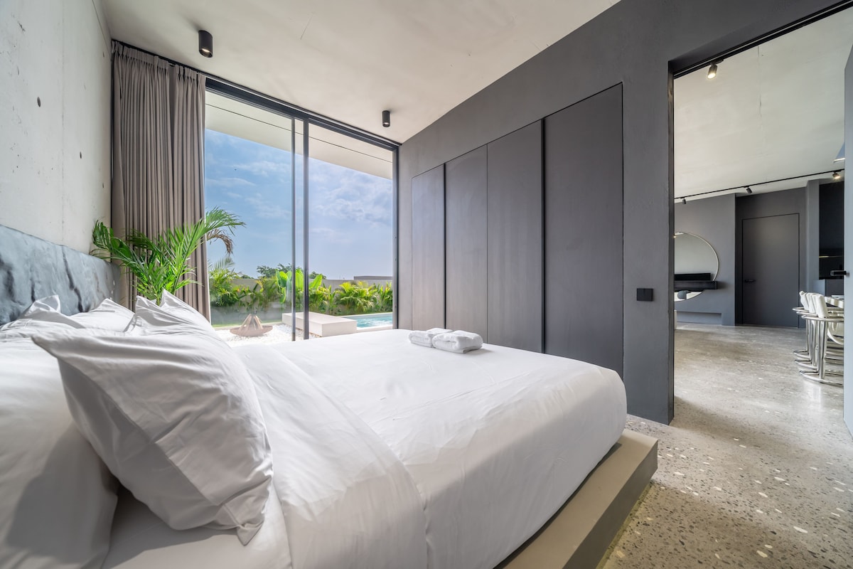 A modern bedroom with a large bed, a view of a swimming pool, and a separate bathroom area.