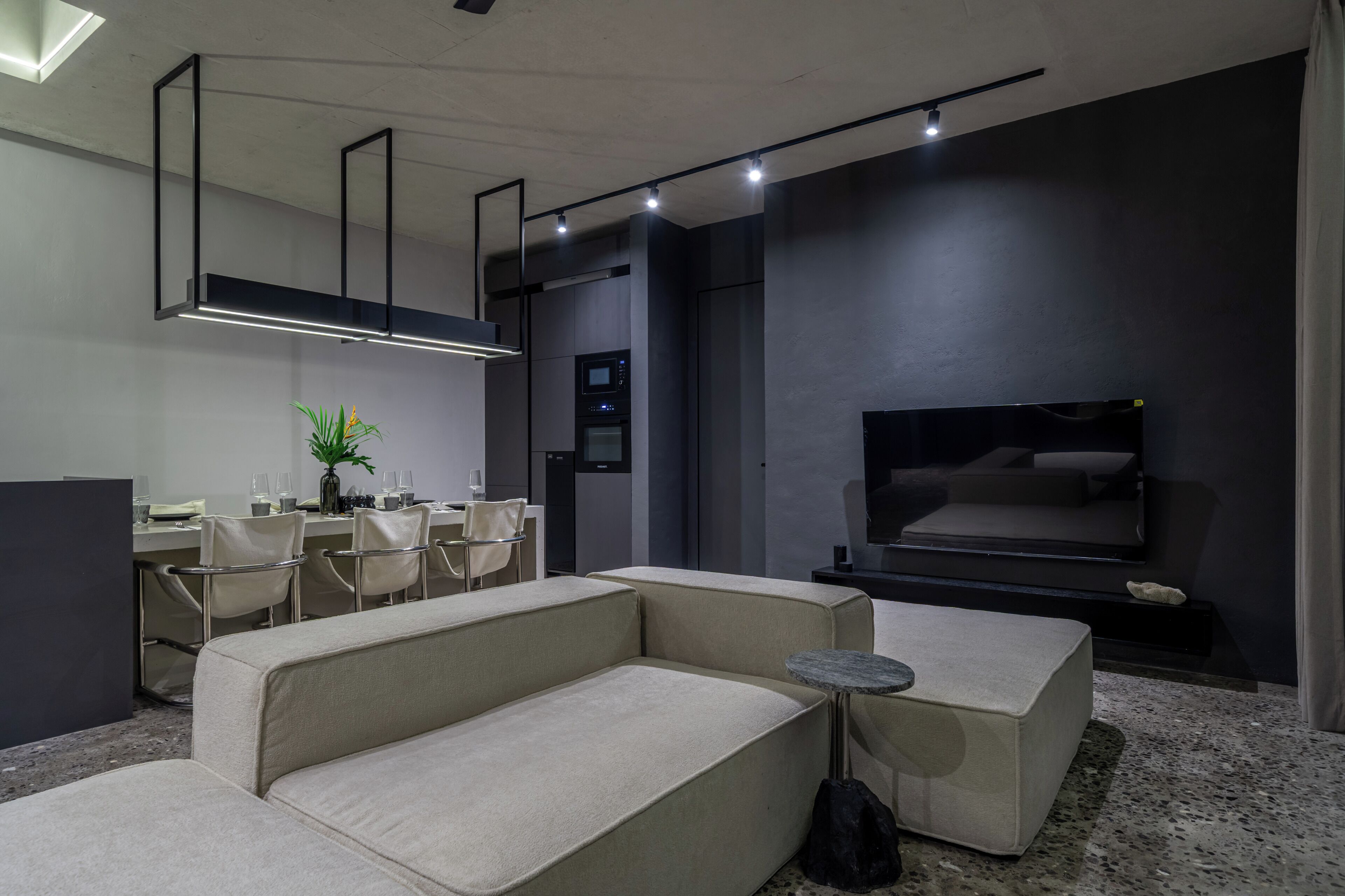 Una sala de estar moderna con un sofá seccional, un comedor con sillas, un televisor de pantalla plana y electrodomésticos empotrados.