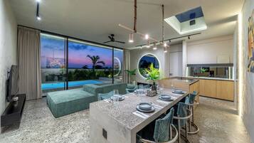 A modern interior with a dining area, kitchen, and a view of a swimming pool.