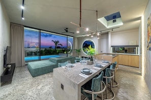 A modern interior with a dining area, kitchen, and a view of a swimming pool. - Predmet Cascade Bali (Tabanan)