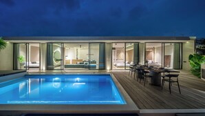 Una casa moderna con piscina, puertas de vidrio que dan a un comedor, y un interior bien iluminado.