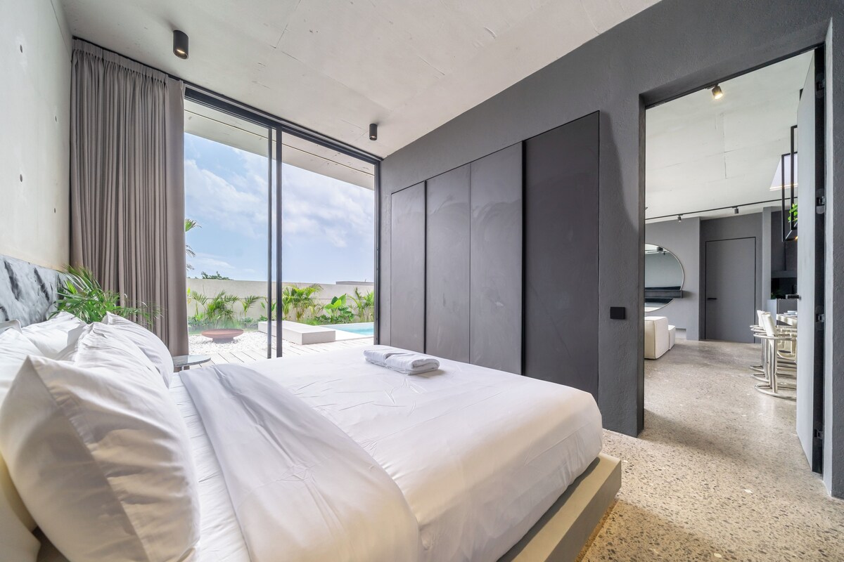 A modern bedroom with a large bed, a view of a swimming pool, and a dining area.