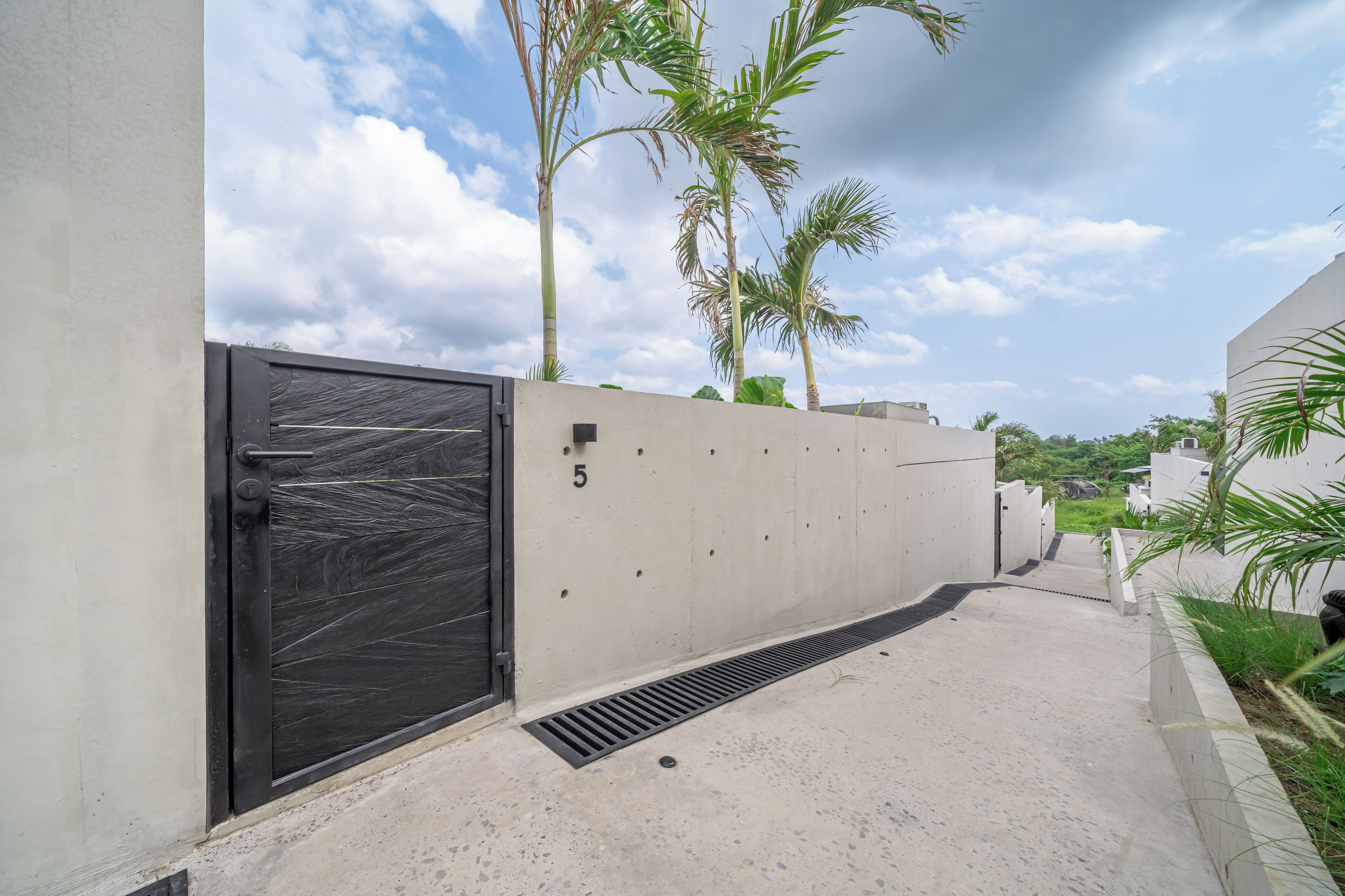 A gated entrance with a concrete wall, a metal door, and a number '5' on the wall.