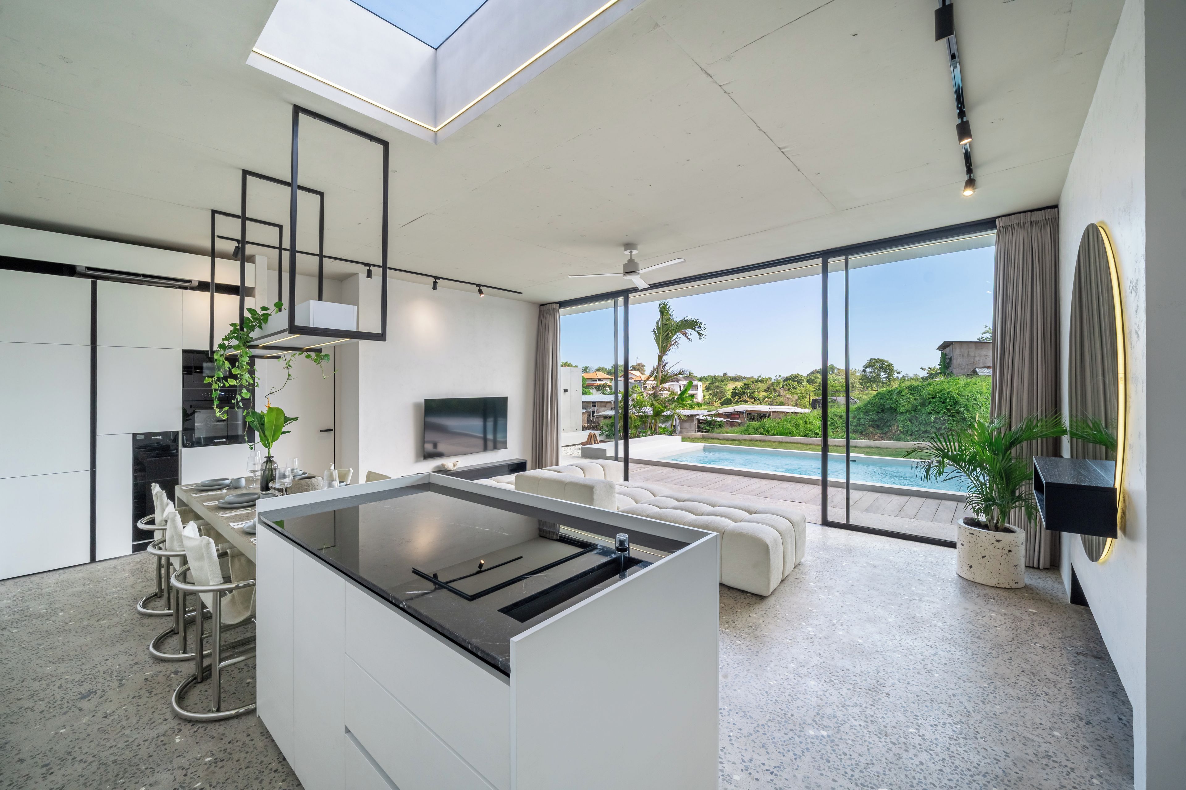 A modern kitchen with a central island, a dining area with a pool view, and a living space with a large window overlooking the outdoors.