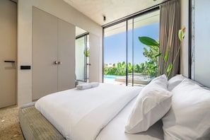 A hotel room with a large bed, a sliding glass door leading to a pool, and a view of greenery. - Predmet Cascade Bali (Tabanan)