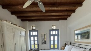 A bedroom with a bed, a wardrobe, a ceiling fan, and two windows with shutters. - Scalinata Tinos Sophisticated Living (Tinos)