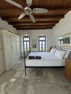 A bedroom with a bed, a wardrobe, a ceiling fan, and two windows with shutters. - Scalinata Tinos Sophisticated Living (Tinos)