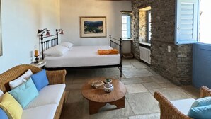 A cozy room with a bed, wicker furniture, a ceiling fan, stone walls, and a stone floor. - Scalinata Tinos Sophisticated Living (Tinos)